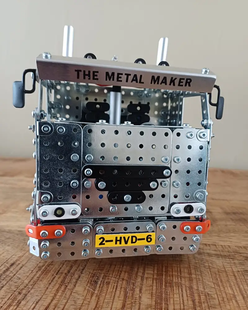 Front view of a metal construction kit robot with perforated steel plates and a sign reading 'THE METAL MAKER' on top.