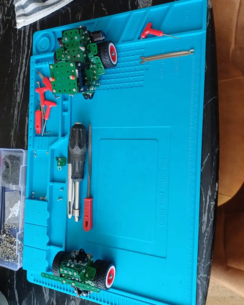 Small robotic chassis built from green metal plates on a blue work mat, with wheels and tools nearby (screwdriver, pliers).