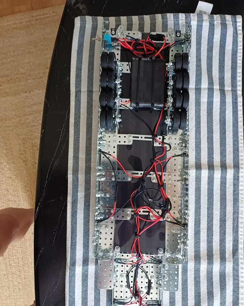 DIY robotic chassis with four wheel assemblies and exposed wiring on a metal frame on striped fabric.